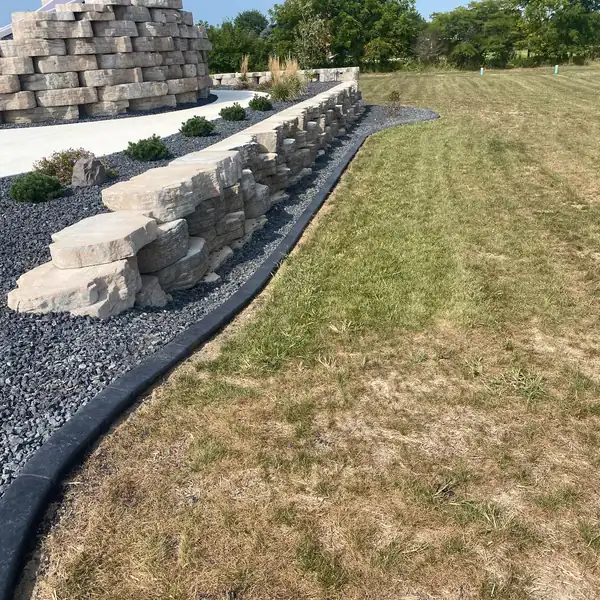 Concrete curb along a rock bed beside a stacked stone wall