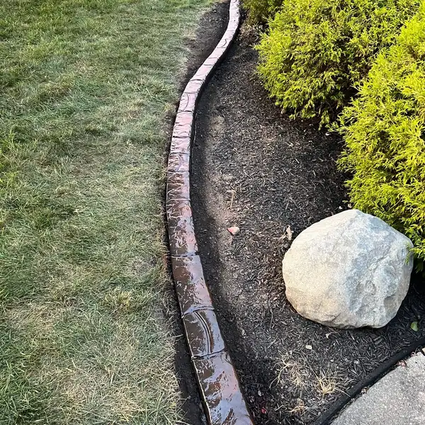 Concrete curb along a bed with shrubs and a boulder