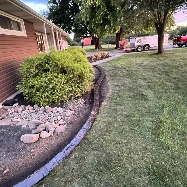 Concrete curb along a rock bed with a shrub beside a brick house